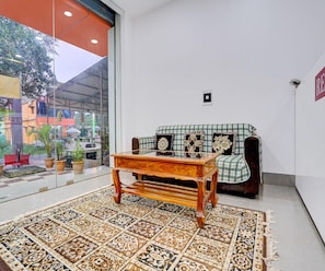 A room with a checkered rug, a wooden table, a sofa with patterned cushions, and a glass wall offering a view of the outside. - Deluxe Hotel Sunshine (Gop)