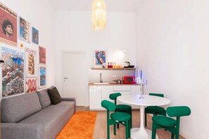A compact living space with a kitchenette, a dining area with green chairs, a grey sofa, and a variety of colorful posters on the walls. - New Listing (Napoli)