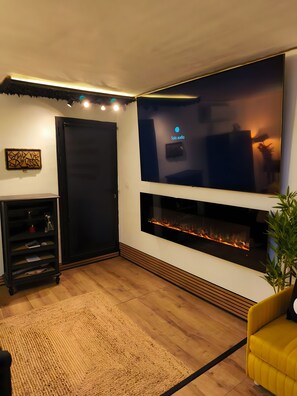 Una sala de estar moderna con un televisor de pantalla plana grande, una chimenea, un mueble de entretenimiento negro y un sofá amarillo.