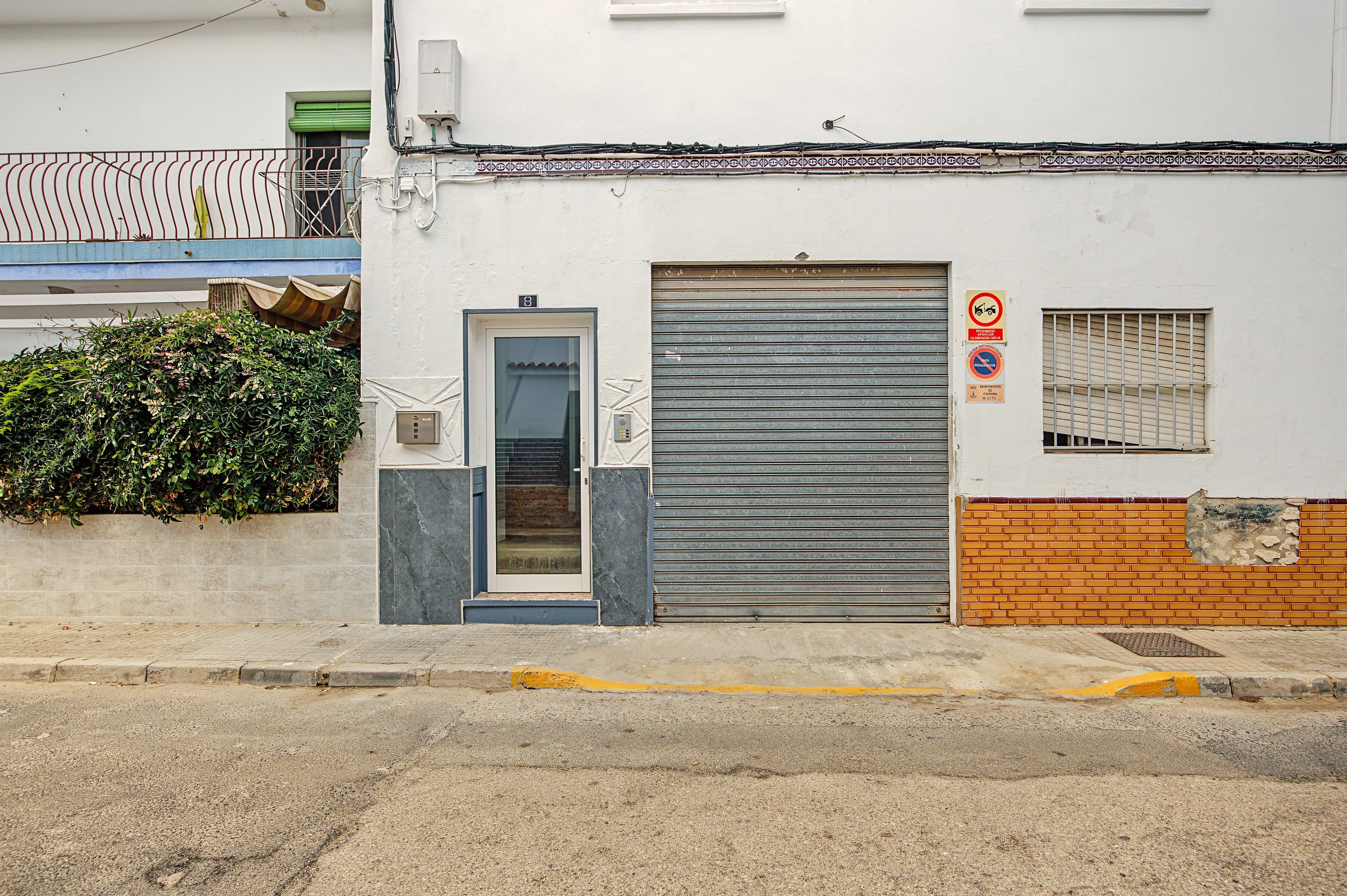 Un edifici amb una persiana metàllica abaixada, una petita finestra amb una reixa de protecció i una tenda verda sobre una escala.