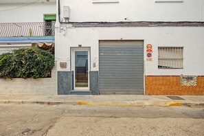 Un edifici amb una persiana metàllica abaixada, una petita finestra amb una reixa de protecció i una tenda verda sobre una escala.