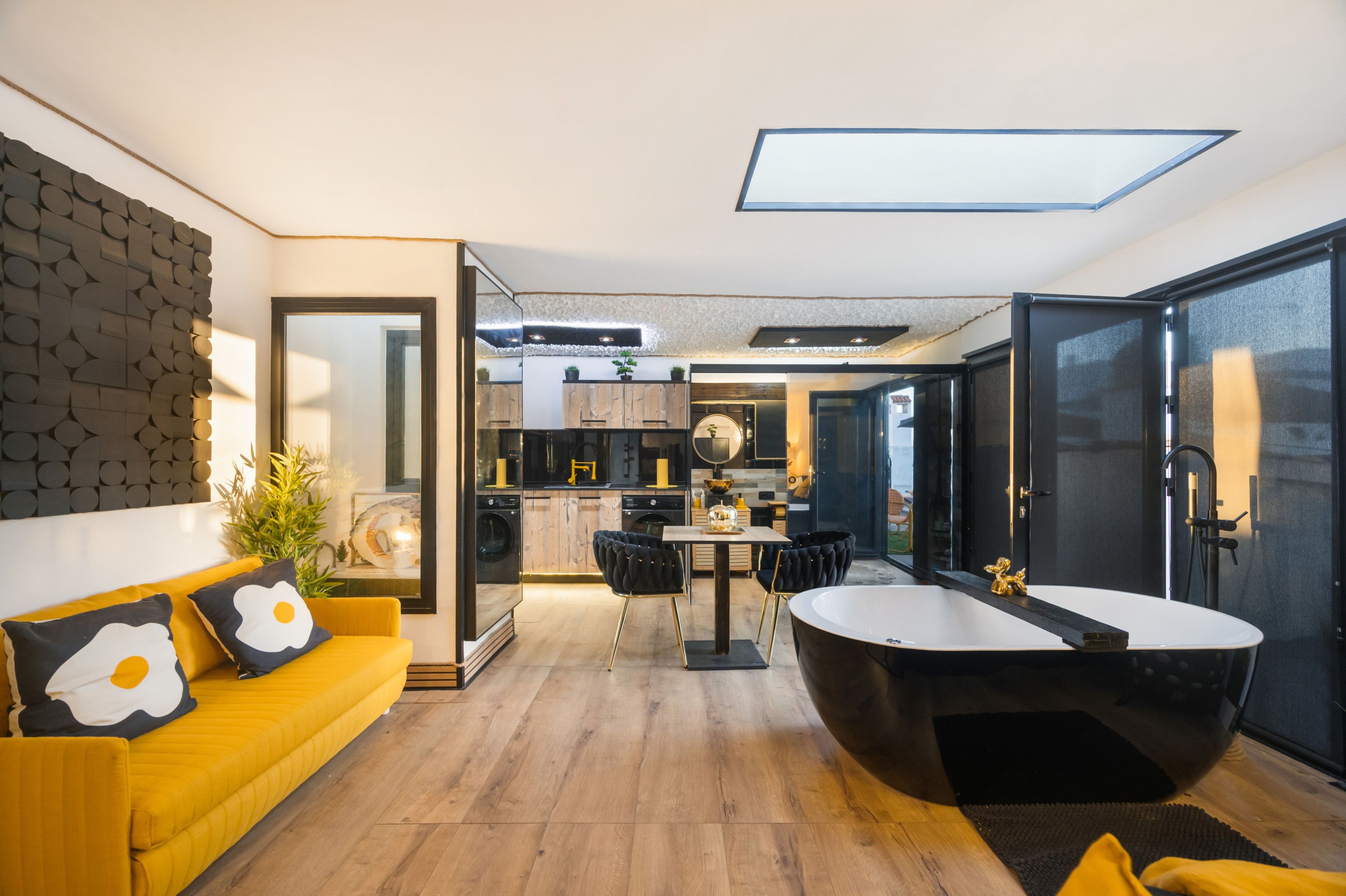 A modern interior with a yellow sofa, a black bathtub, and a kitchen area.