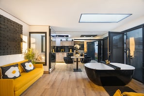 Un interior modern amb un sofà groc, una banyera negra i una zona de cuina.