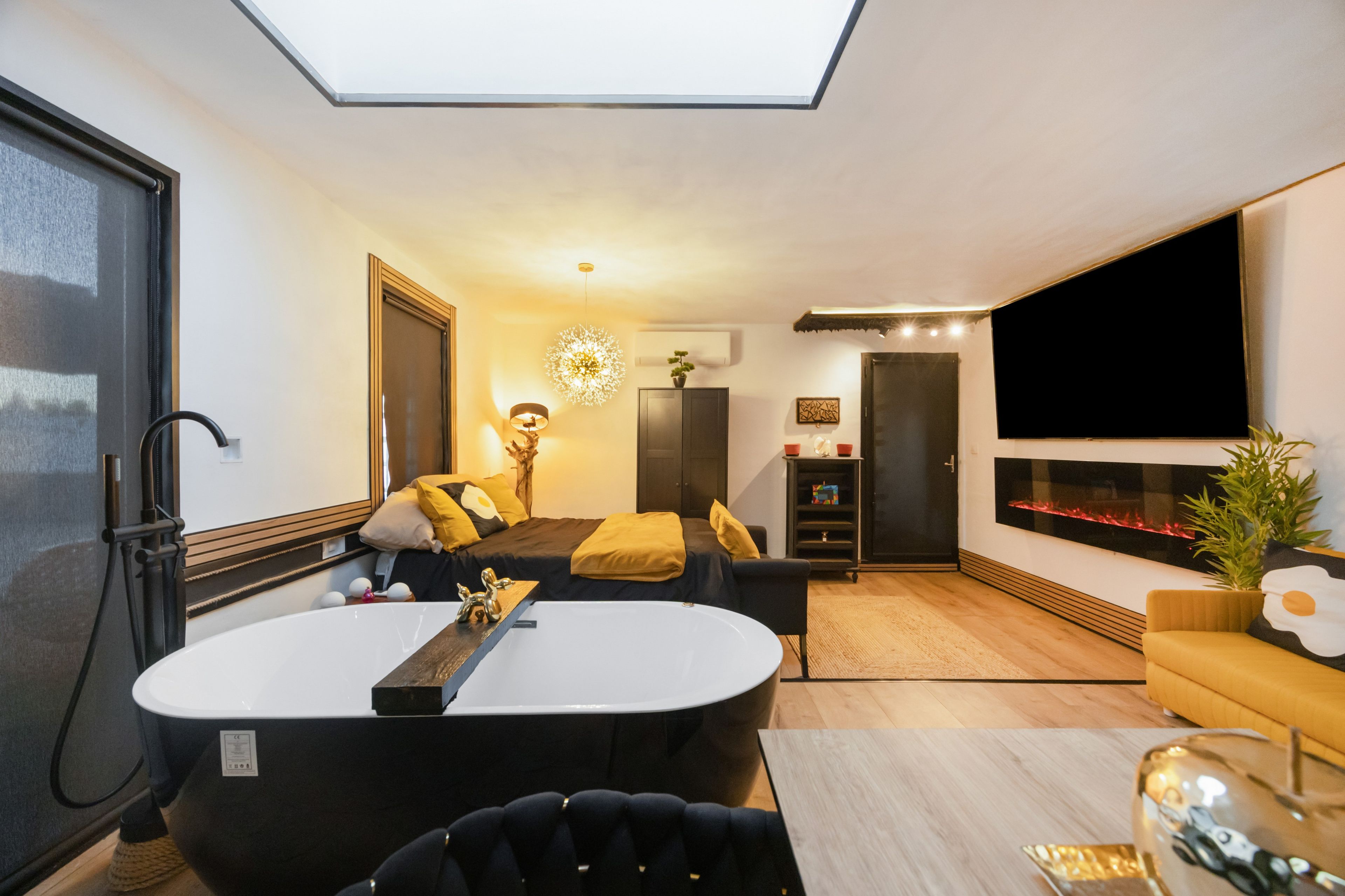 A modern living room with a large flat-screen TV, a fireplace, and a skylight.