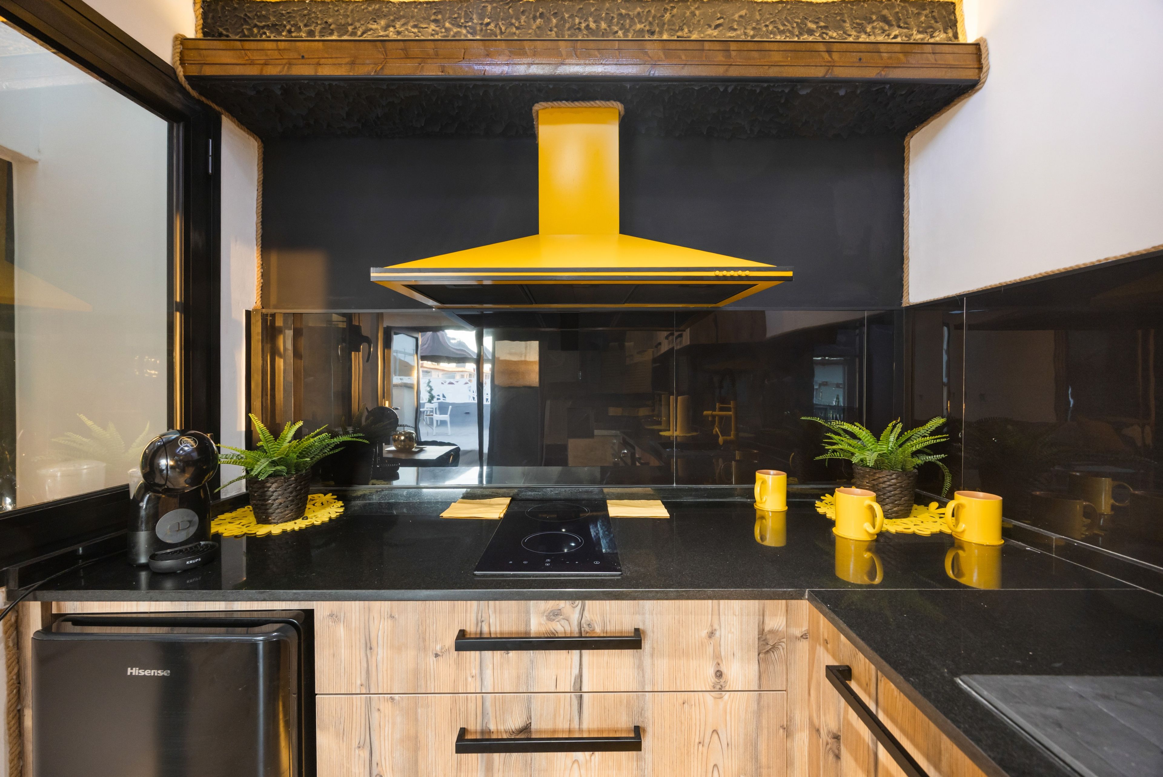 A modern kitchen with a black countertop, wooden cabinets, a stainless steel dishwasher, and a yellow range hood.