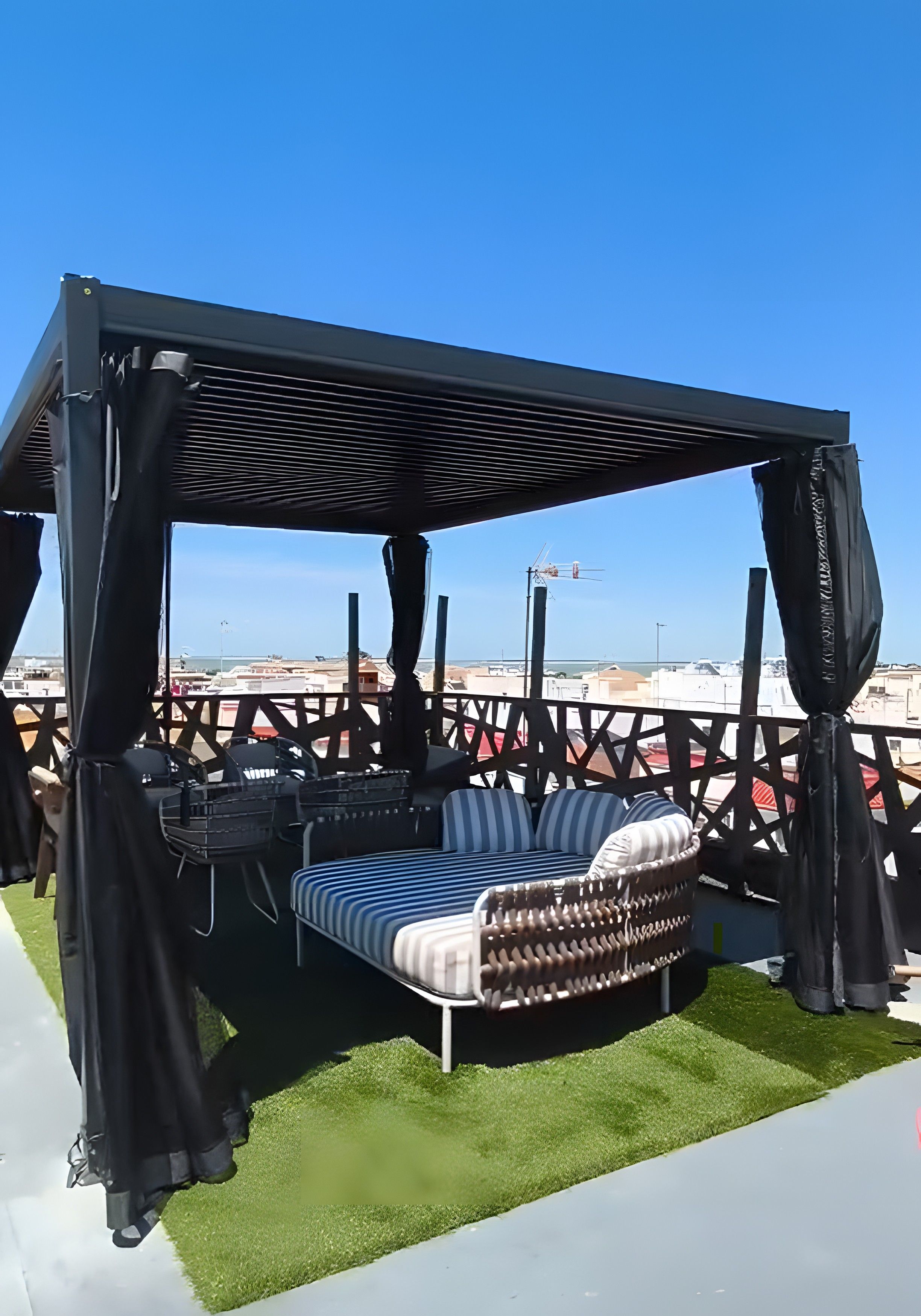 A rooftop seating area with a canopy, a cushioned bench, and a view of the cityscape.
