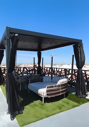 Un área de estar en la azotea con un toldo, un banco acolchado y vistas a la ciudad.