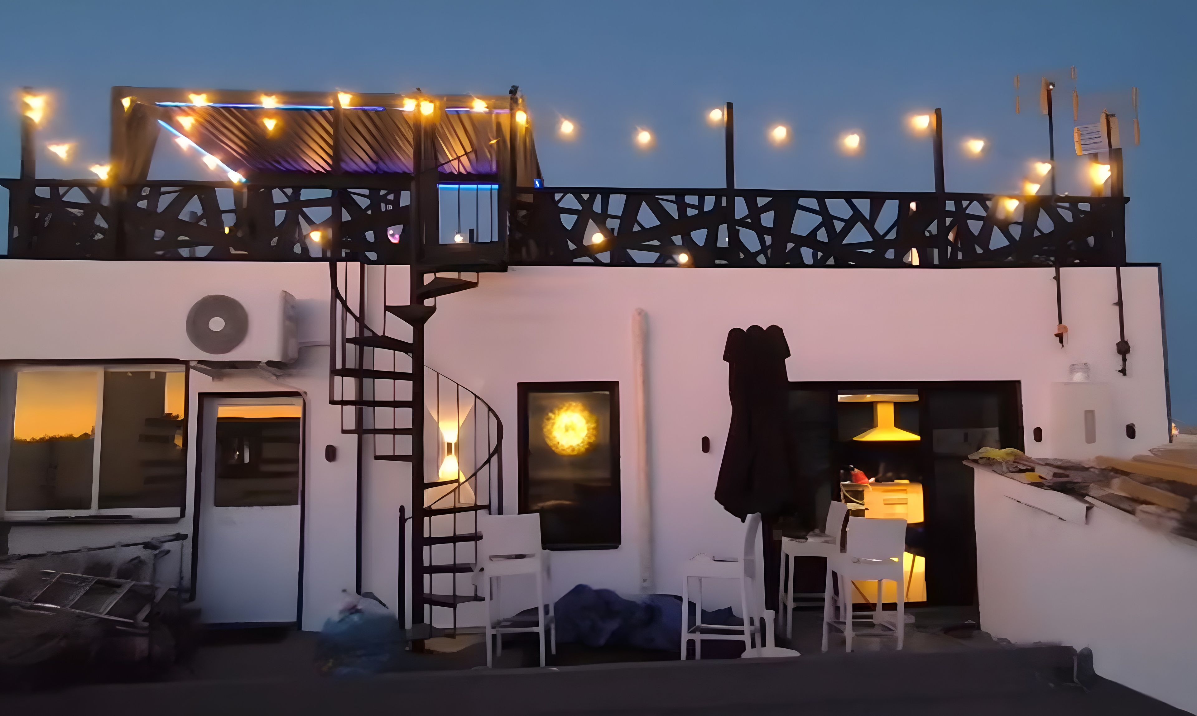 A rooftop terrace with string lights, a staircase, and a table with chairs.