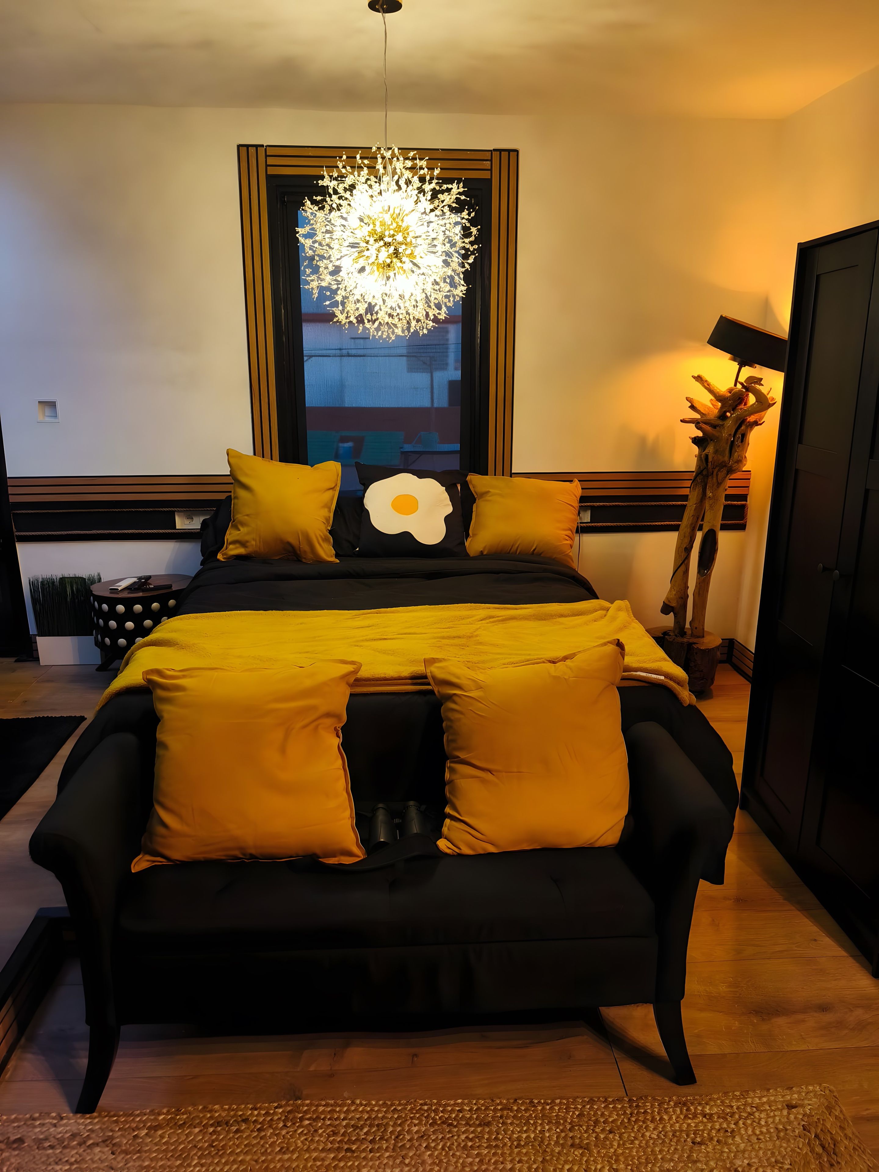 A bedroom with a bed, a bedside lamp, a window, and a decorative plant.