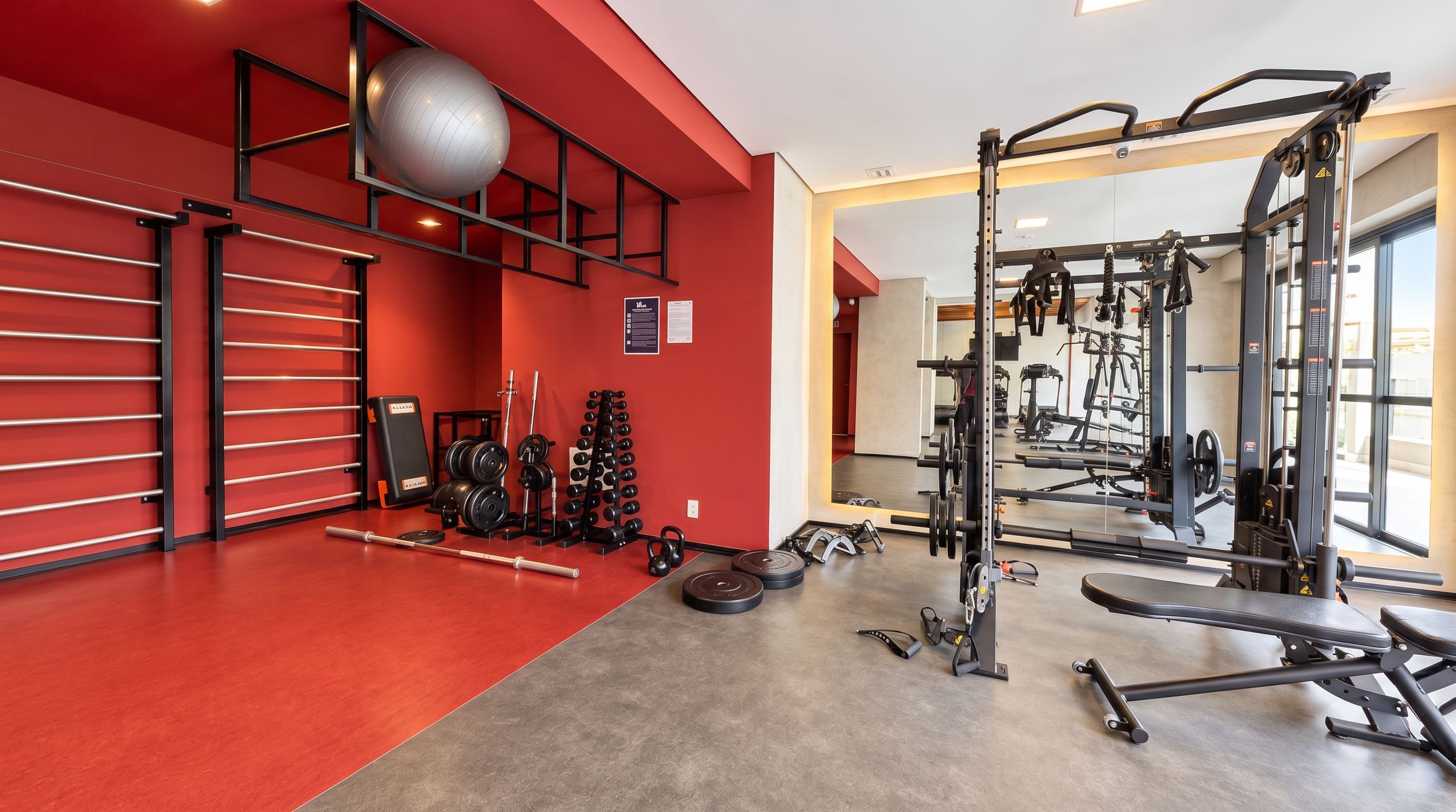 Un gimnasio con paredes rojas, equipo de levantamiento de pesas y un espejo grande.