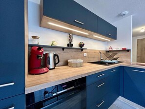A modern kitchen with a wooden countertop, built-in appliances, and blue cabinetry. - 3rd floor, view panoramic, terrace, tv, 68m², Serre Chevalier (Briançon)