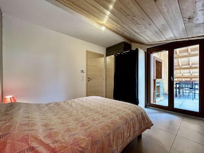 Un dormitorio con cama, armario, puerta y vistas a un espacio exterior con mesa y sillas a través de una puerta de cristal.