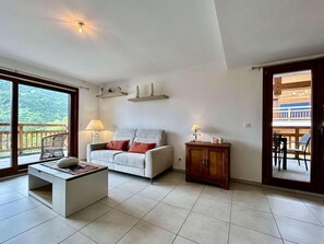 A living room with a sofa, coffee table, and a cabinet. There is a balcony with a view of greenery. - 3rd floor, view panoramic, terrace, tv, 68m², Serre Chevalier (Briançon)