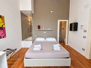 A modern hotel room with a bed, a bathroom with a shower, and a TV mounted on the wall. - Lo Schiaccianoci B&B (Taranto)