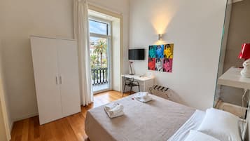 Une chambre d’hôtel équipée d’un lit, d’un bureau, d’une chaise, d’une télévision et d’un balcon offrant une vue sur les palmiers.