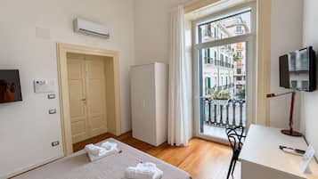 Ein Hotelzimmer mit Bett, Schreibtisch, Fernseher und einem Balkon mit Blick auf Gebäude sowie einer Klimaanlage.