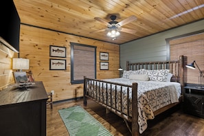 A wooden cabin bedroom with a bed, a desk, a lamp, and framed fish pictures on the wall. - Family Lodge in Aska: Mountain Views, Hot Tub, Waterfall & Kids’ Bunk Room (Blue Ridge)