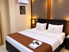 Ein Hotelzimmer mit einem Bett, einem Nachttisch mit Telefon, einem Bild an der Wand und einer Klimaanlage.