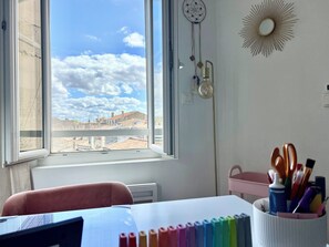 A room with a large window, a desk with a computer, a chair, and a wall-mounted dreamcatcher. - New Listing (Bordeaux)