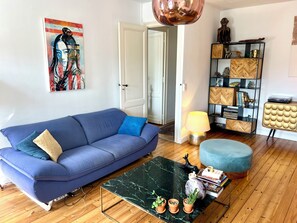 A living room with a blue sofa, a coffee table, a lamp, a bookshelf, and a door. - New Listing (Bordeaux)