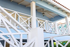 Ein weißer Balkon mit einem geometrischen Geländer, einer blauen Wand und einem geflasterten Dach.