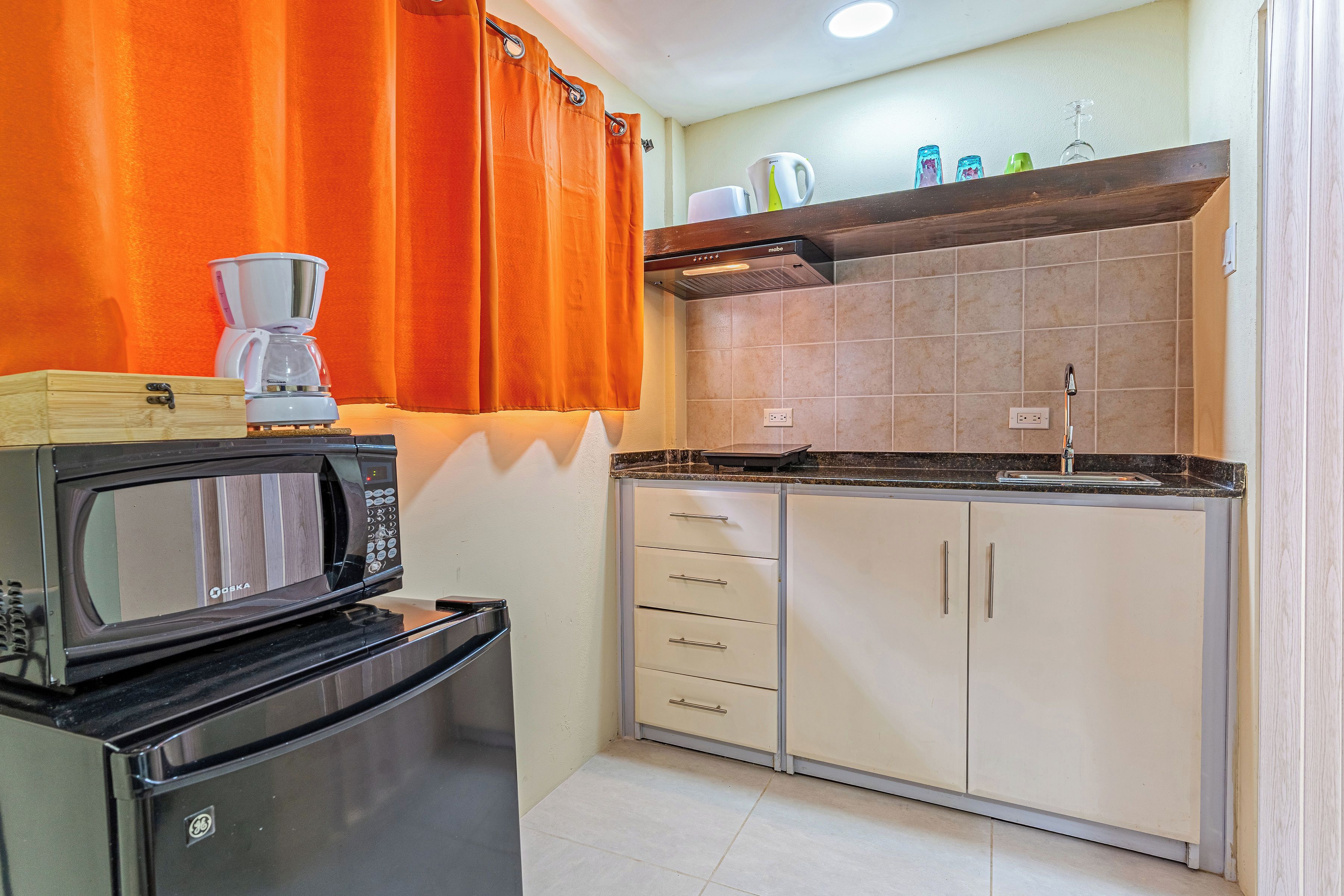 A compact kitchen with a microwave, a coffee maker, and a kettle on the counter.