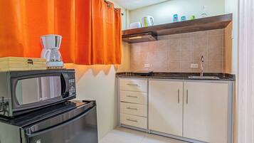 A compact kitchen with a microwave, a coffee maker, and a kettle on the counter.