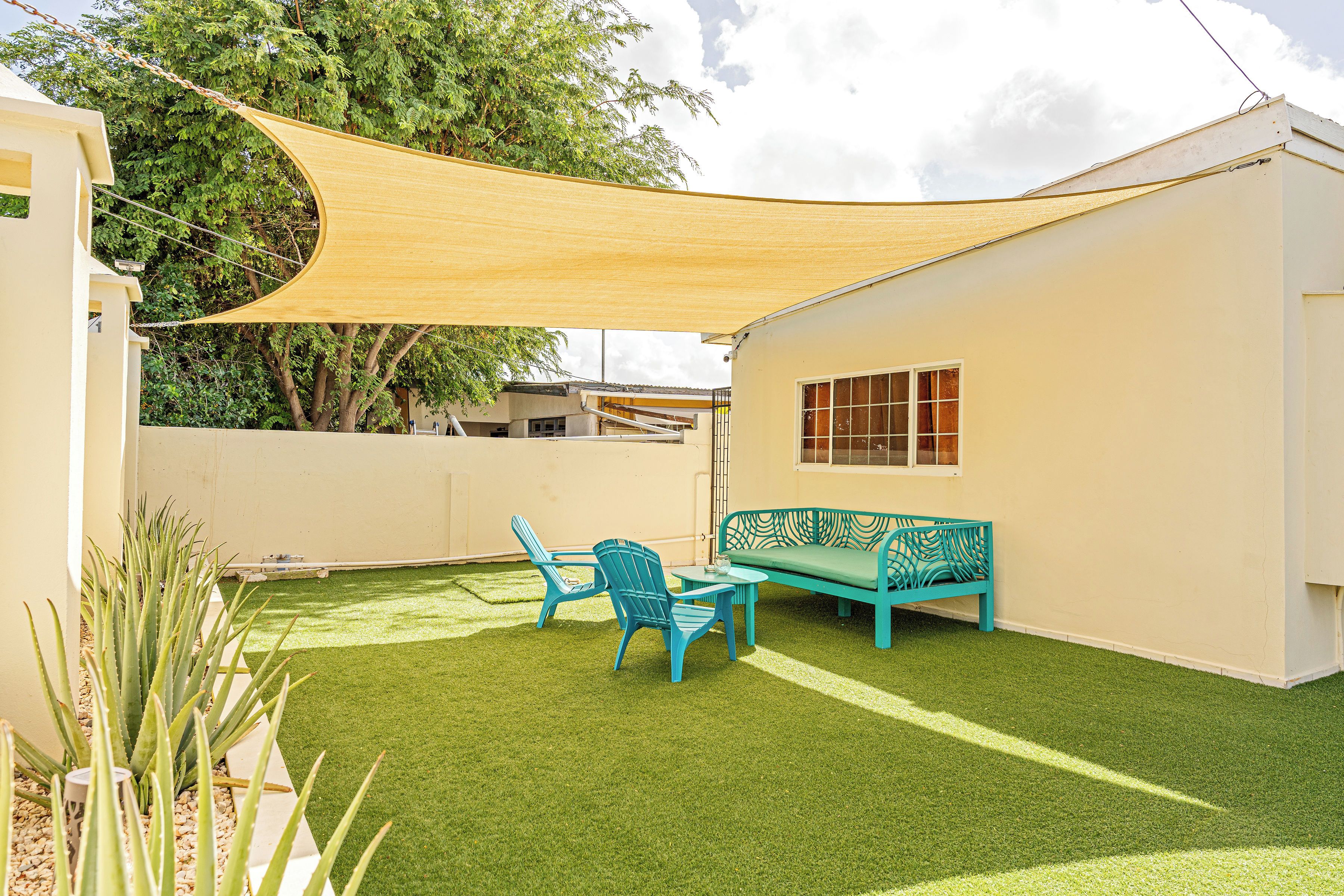 Eine Terrasse mit einer Sitzecke, Tischen und Kunstgraseinsatz, beschattet durch ein Sonnensegel.