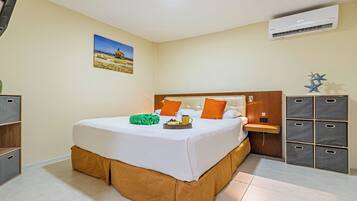 A hotel room with a bed, a bedside table, a dresser, and an air conditioning unit.