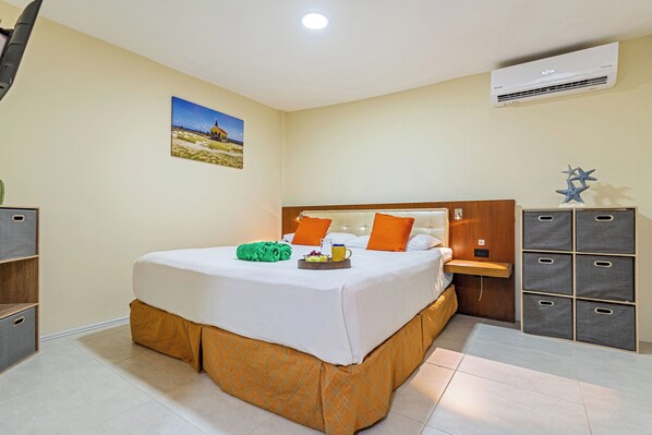 A hotel room with a bed, a bedside table, a dresser, and an air conditioning unit. - IslaRita Stays #6 spacious studio near Eagle Beach (Oranjestad)