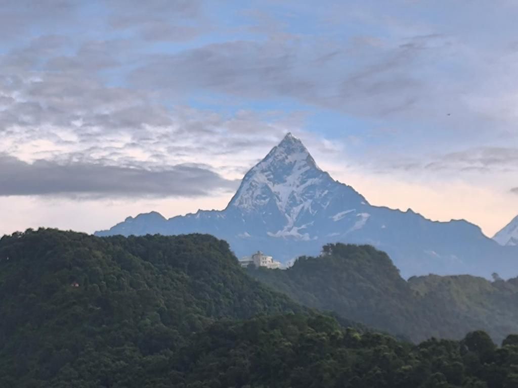 Un paisaje montañoso con un pico destacado, verdes colinas y un edificio pequeño a la izquierda.