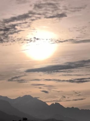 Silueta de una cordillera bajo un sol con nubes.