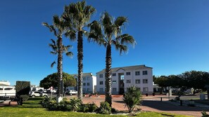 A multi-story building with a flat roof, surrounded by well-maintained palm trees and a clear blue sky. - Perfect 2-bedroom apartment in Big Bay with stunning views (Cape Town)
