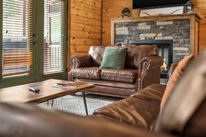A cozy living room with a leather sofa, a coffee table, and a fireplace. - Sleeps 24, Private Heated Indoor Pool, Theater, Arcade, 6.5 Mi to Dollywood (Pigeon Forge)