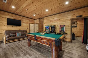 A wooden-paneled room with a pool table, a sofa, and arcade games. - Sleeps 24, Private Heated Indoor Pool, Theater, Arcade, 6.5 Mi to Dollywood (Pigeon Forge)