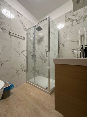 A modern bathroom with a glass-enclosed shower, marble walls, and a wooden vanity. - New Listing (Venezia)