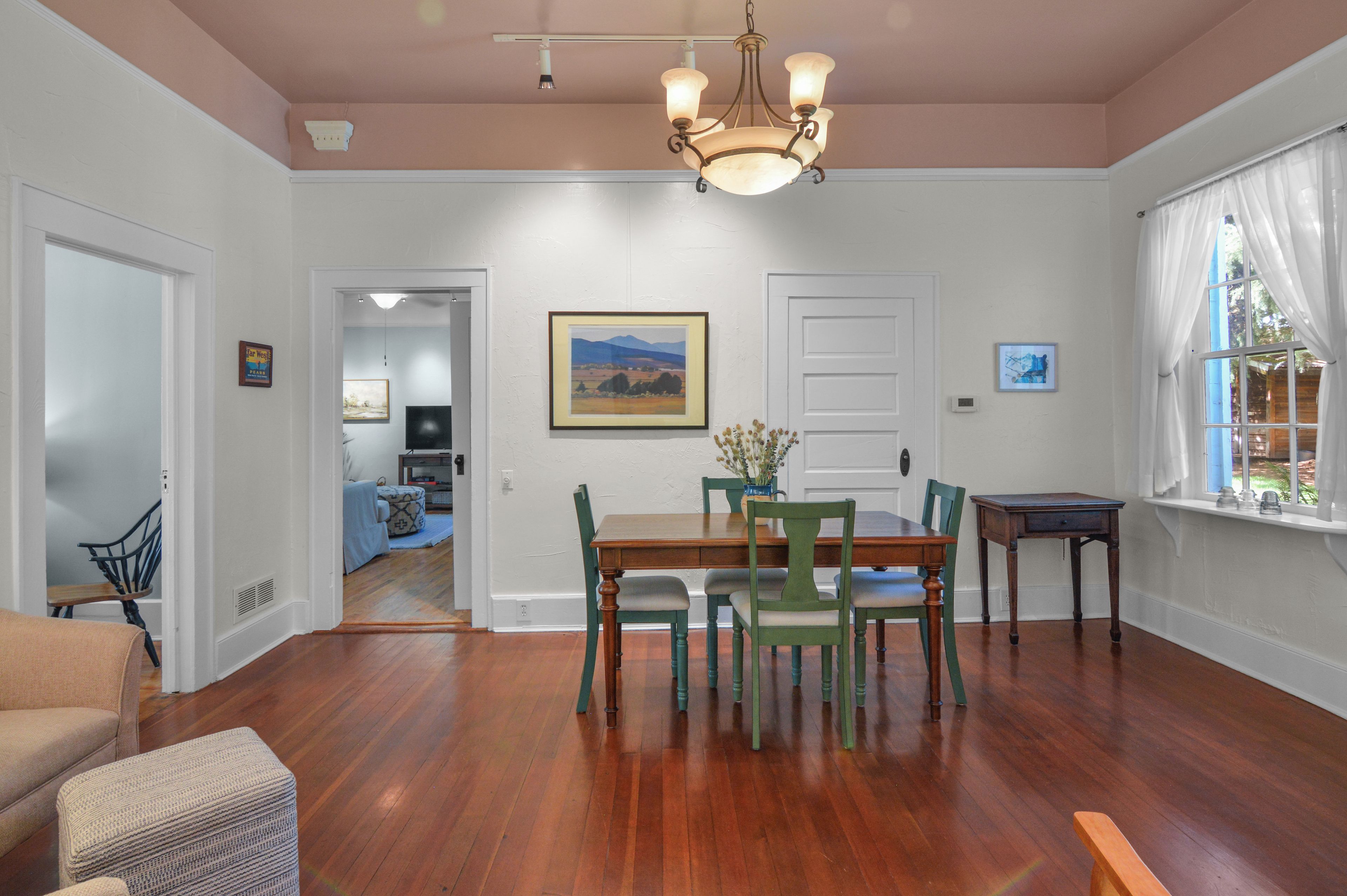 A dining area with a wooden table and chairs, a chandelier, and a painting on the wall.