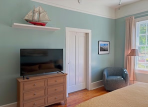 A bedroom with a television on a wooden dresser, a chair, a door, and a window with curtains. - Fabulous 2-bedroom house in charming Jacksonville Oregon (Jacksonville)