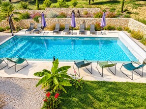 Ein rechteckiger Swimmingpool mit einer Steinmauer und einer Rasenfläche mit Pflanzen und Blumen.