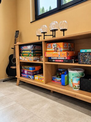 A shelf with various board games and puzzles, a guitar leaning against the wall, and a window above. - New Listing (Le Pègue)