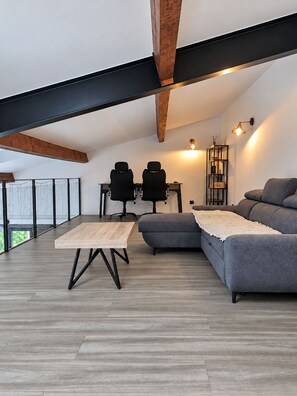 A modern loft with a wooden ceiling, a grey sofa, a wooden coffee table, and two office chairs. - New Listing (Le Pègue)