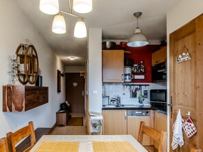 A compact kitchen with wooden cabinets, a built-in oven, and a hanging light fixture. - Apartment with balcony with mountain view (Morillon)