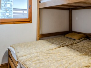 A bunk bed with a wooden headboard, a window with a view of a building, and a plain wall. - Apartment with balcony with mountain view (Morillon)