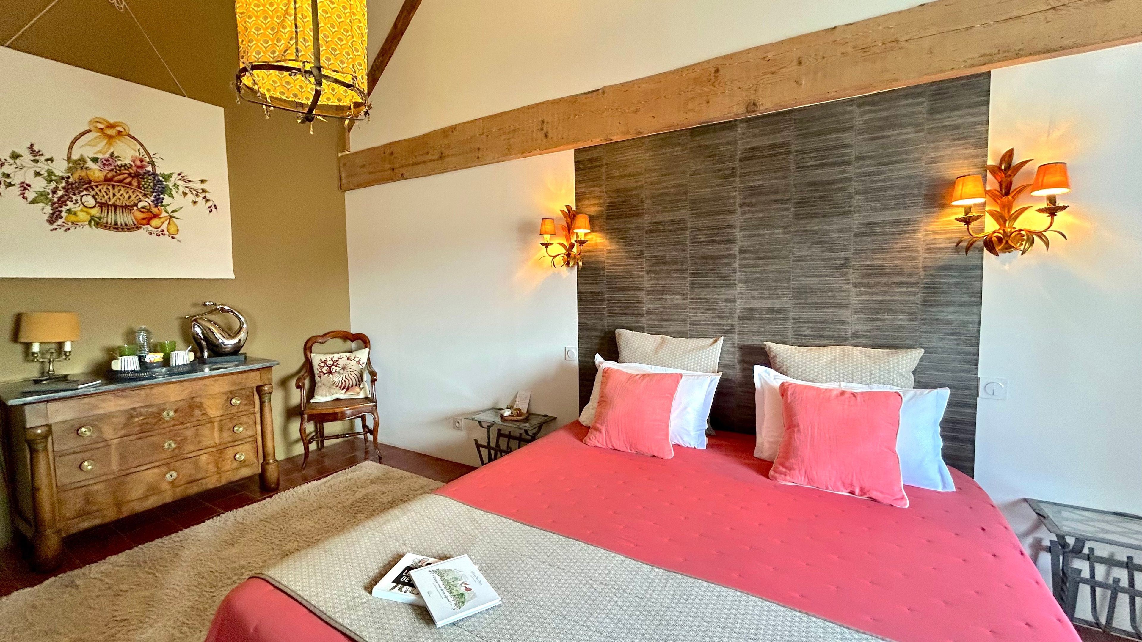 Een slaapkamer met een groot bed, een houten hoofdbord, wandlampen, een dressoir en een decoratief wandobject.