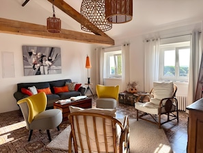 Una sala de estar con sofá, sillones, una mesa de centro, una lámpara y una ventana con cortinas.
