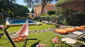 En trädgård med en pool, en hängmatta, solstolar och ett bord.
