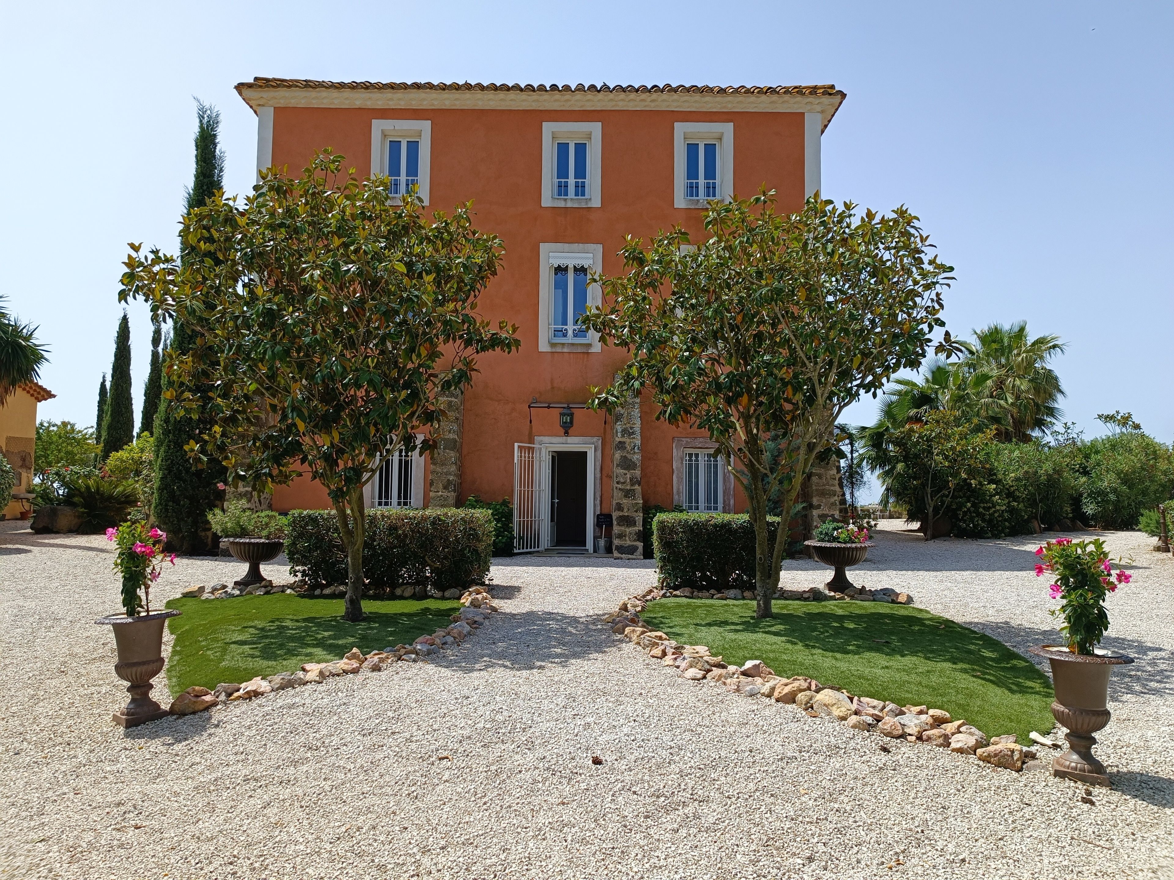 A two-story building with a symmetrical facade, a gravel driveway, and a well-maintained garden with shrubs and flowering plants.