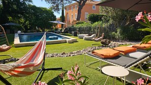 Um quintal com piscina, rede, cadeiras de descanso e mesa.