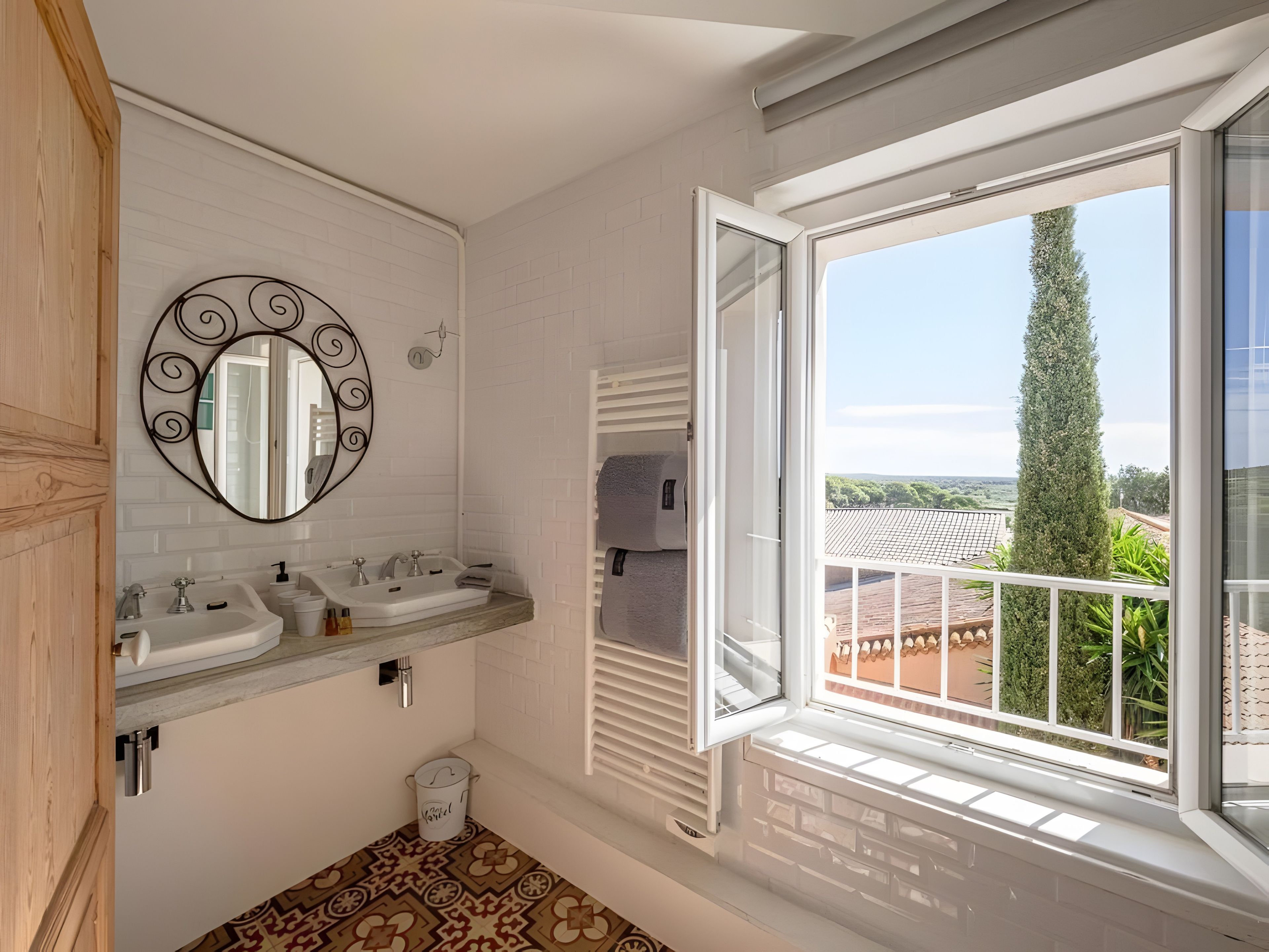 Een badkamer met twee wastafels, een spiegel en een raam met uitzicht op een balkon en bomen.