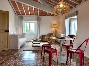 A living room with a sofa, a dining table with chairs, a lamp, and a view of the outdoors. - Apartment 'Suite Grand Duc - Vue Mer' with Wi-Fi and Air Conditioning (Portiragnes)